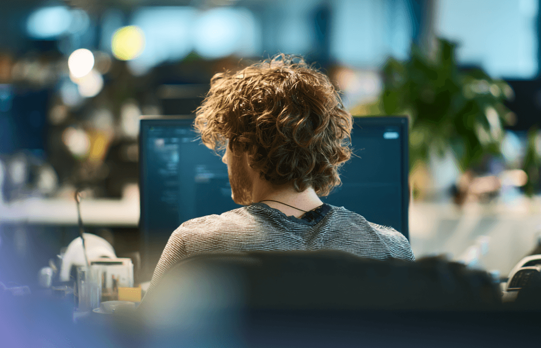 Oversikt over en utvikler med krøllete hår som jobber på en datamaskin på et moderne kontor.